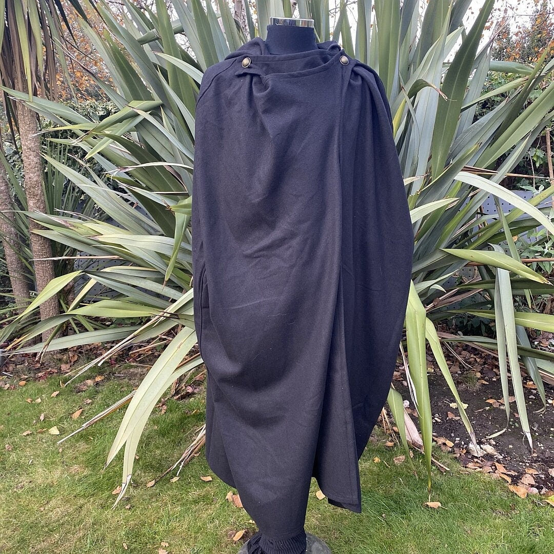 Black medieval cloak draped over mannequin amidst garden shrubs for LARP.