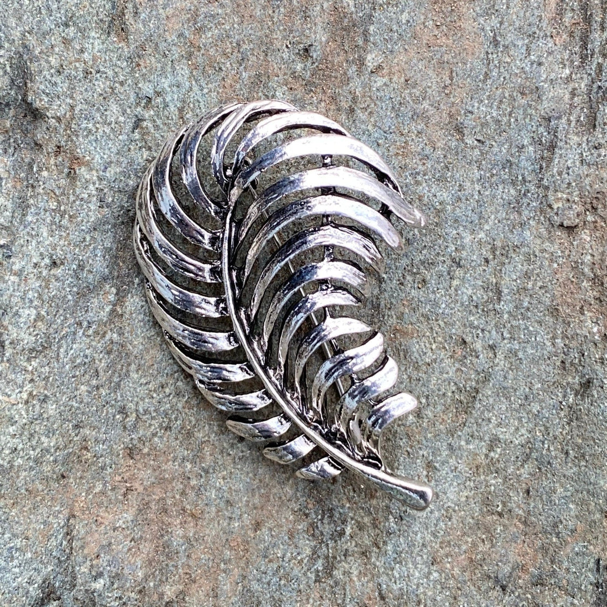 Dark silver fern brooch on stone, medieval LARP accessory, side angle view.