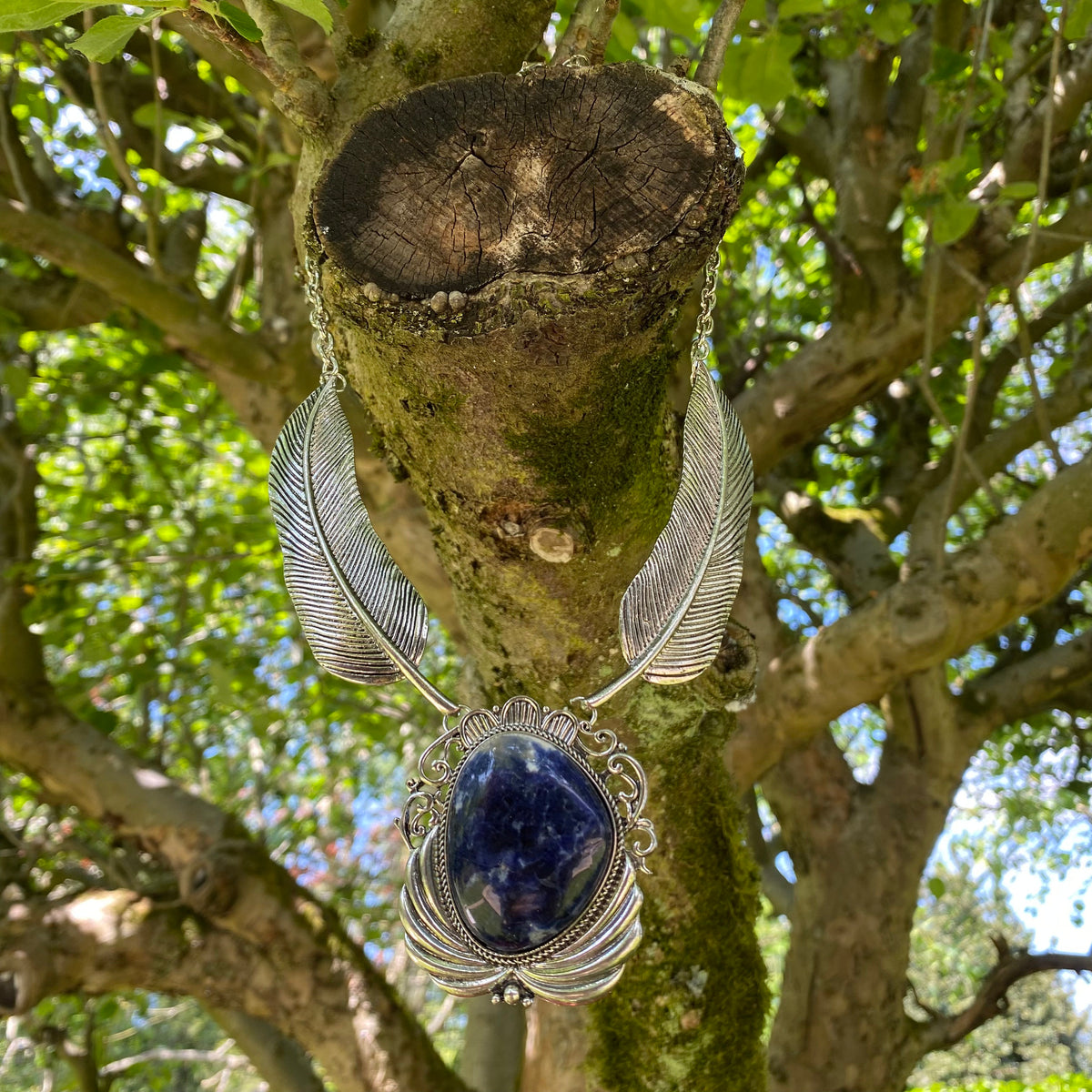 Silver feather necklace with lapis lazuli, hanging on a tree for LARP.