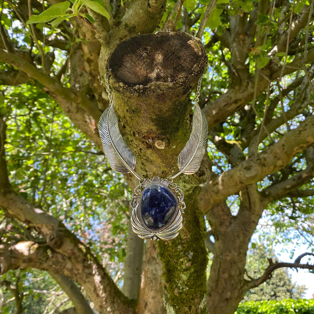 Necklace with lapis lazuli and feather detail hanging on tree branch, medieval LARP.