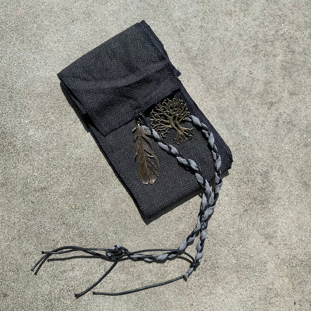 Dark grey medieval LARP sash with feather and tree charms in sunlight.